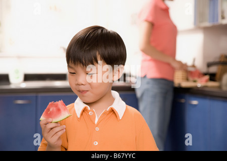 Close-up of a Boy eating watermelon avec sa mère derrière lui Banque D'Images
