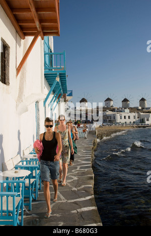 Les femmes se promener le long des restaurants et bars en banque, les moulins à vent en arrière-plan, la Petite Venise, Mykonos-Town, Mykonos, Grèce Banque D'Images