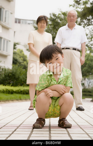 Portrait d'un garçon accroupi et ses grands-parents se tenant derrière lui Banque D'Images