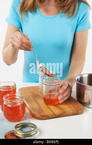 Woman Pouring gelée aux poivrons rouges en bocaux Banque D'Images