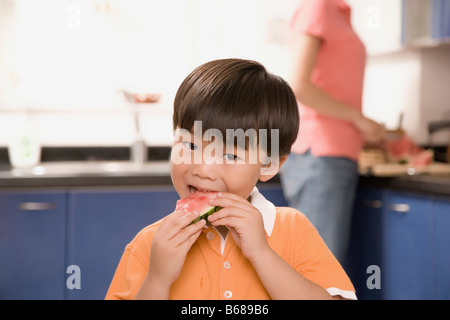 Close-up of a Boy eating watermelon avec sa mère derrière lui Banque D'Images