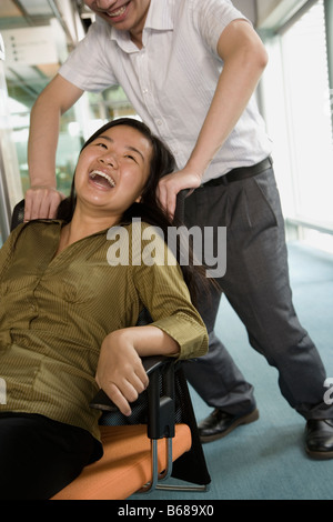 Jeune homme poussant une jeune femme assise sur une chaise Banque D'Images