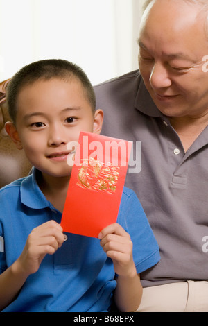 Portrait d'un garçon assis avec son grand-père et tenant une enveloppe cadeau rouge Banque D'Images