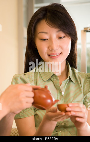 Close-up of a person's hands pouring dans une tasse de thé tenue par une jeune femme Banque D'Images