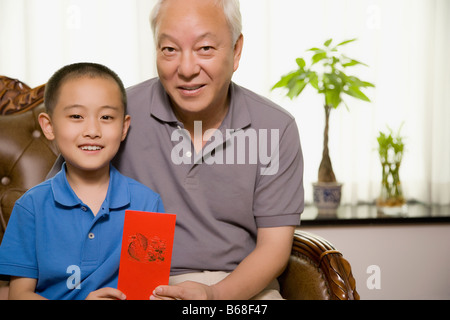 Portrait d'un garçon assis avec son grand-père et tenant une enveloppe cadeau rouge Banque D'Images