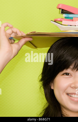 Portrait of a young woman carrying papeterie de bureau sur sa tête et souriant Banque D'Images