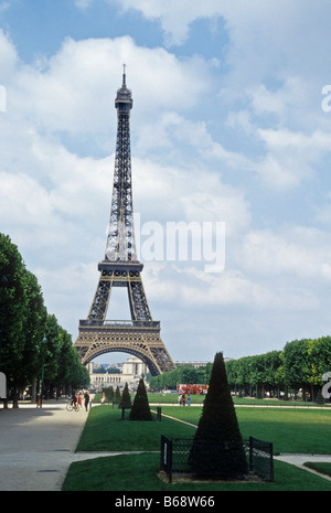 La Tour Eiffel, Paris, contre ciel nuageux Ciel bleu avec de l'herbe et les arbres le parc du Champ-de-Mars. Banque D'Images