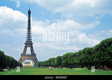 La Tour Eiffel, Paris, contre ciel nuageux Ciel bleu avec de l'herbe et les arbres le parc du Champ-de-Mars. Banque D'Images