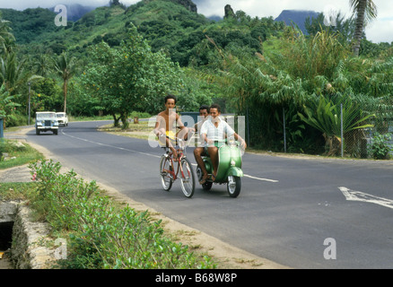 Teen boy sur le vélo d'être sollicités par d'autres garçons sur scooter Pacifique du Sud , Pacifique Moorea, Tahiti Banque D'Images