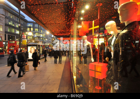 Shoppers on trottoir devant department store/windows avec des cadeaux de Noël sur l'affichage à l'Oxford Street avec des lumières de Noël dans la région de West End de Londres UK Banque D'Images