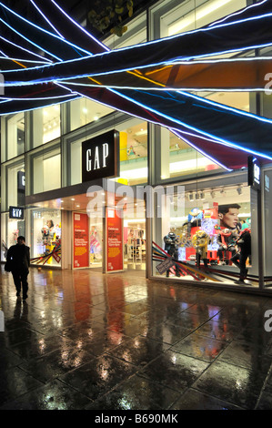 Des clients mouillés à l'extérieur de la boutique de vêtements Gap et de la fenêtre avant de la boutique Oxford Street London West End à la nuit les gens Noël shopping Sous la pluie Angleterre Royaume-Uni Banque D'Images