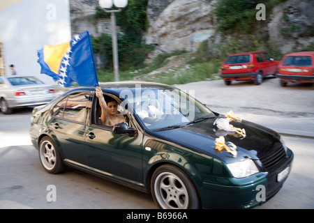 La Bosnie-et-Herzégovine voiture en mouvement dans une ville et une fille de la rue drapeau bosniaque vagues hors de la fenêtre de voiture Banque D'Images