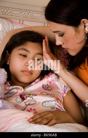 Sentiment mère hispanique le front de sa fille malade d'une fièvre pendant qu'elle est dans le lit de pose en pyjama. Banque D'Images