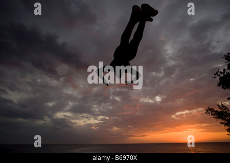 La Jamaïque Negril Silhouette de jeune homme sautant de falaise au-dessus de la grotte des Pirates Banque D'Images