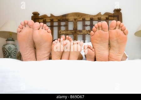 Plante de couple et leurs enfants et les pieds sur le lit Banque D'Images