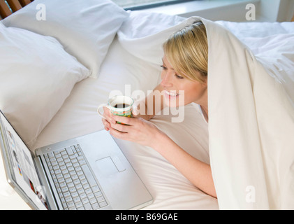 Femme working on laptop in bed Banque D'Images