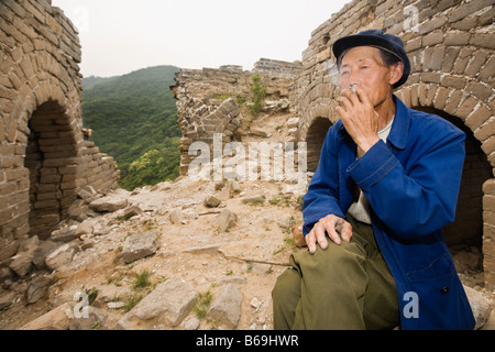 Man fumeurs sur un mur, et la Grande Muraille de Chine, Beijing, Chine Banque D'Images