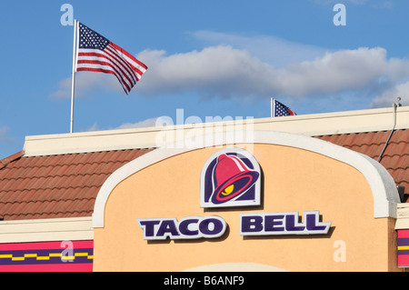 Taco Bell Logo et signe sur l'extérieur du restaurant avec le drapeau américain sur le poteau en arrière-plan. Banque D'Images