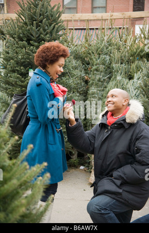 African man giving girlfriend bague de fiançailles dans beaucoup d'arbres de Noël Banque D'Images