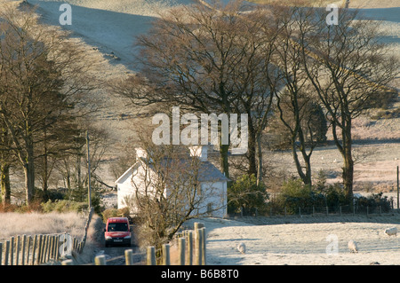 Bureau de poste rouge van de livraison de courrier portant à une maison rurale isolée sur un matin d'hiver près de Pontrhydygroes Mid Wales UK Banque D'Images