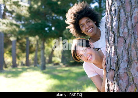 Jeune femme et l'homme à la recherche de derrière un tronc d'arbre Banque D'Images