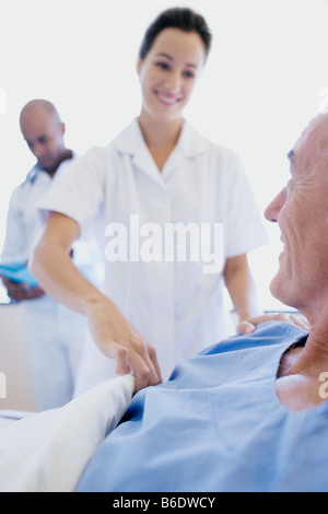 Les soins aux patients. Infirmière ayant tendance à un patient dans un hôpital alors qu'un médecin vérifie les notes médicales du patient. Banque D'Images