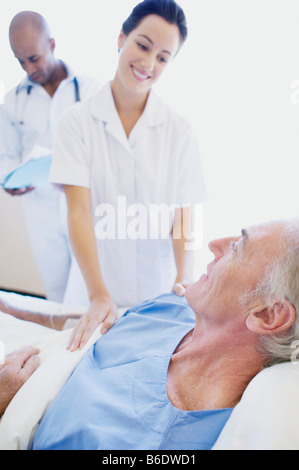 Les soins aux patients. Infirmière ayant tendance à un patient dans un hôpital alors qu'un médecin vérifie les notes médicales du patient. Banque D'Images