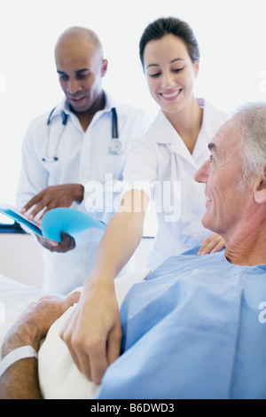 Les soins aux patients. Infirmière ayant tendance à un patient dans un hôpital alors qu'un médecin vérifie les notes médicales du patient. Banque D'Images