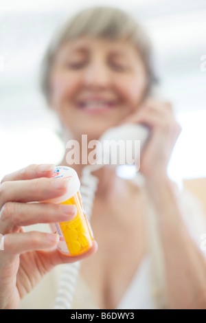 Comprimés. Femme lisant les instructions sur un pot de pilules tout en parlant sur un téléphone. Banque D'Images