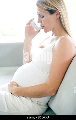 Femme enceinte asthmatique à l'aide d'un inhalateur pour traiter une crise d'asthme. Banque D'Images