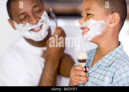 Père et fils avec de la mousse sur le visage. Le père est le rasage alors que son fils est chant dans un blaireau. Banque D'Images