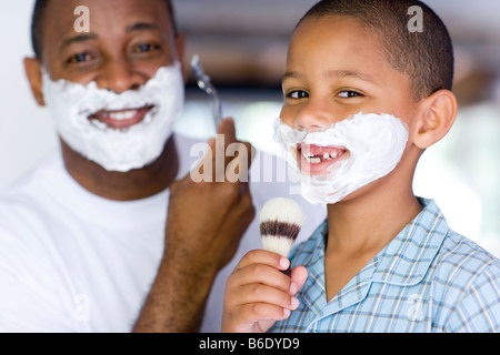 Père et fils avec de la mousse sur le visage. Le père est le rasage alors que son fils est chant dans un blaireau. Banque D'Images