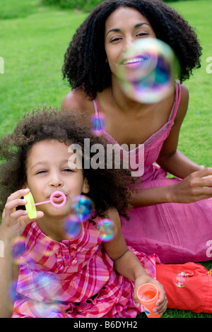 Mère et fille, assis sur l'herbe, souffler des bulles de savon. Banque D'Images