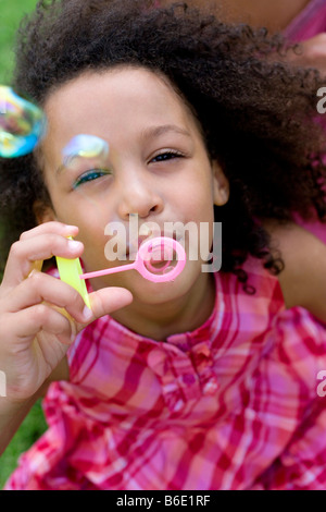 Girl blowing des bulles de savon grâce à une baguette. Banque D'Images