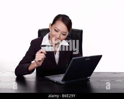 Businesswoman using laptop holding credit card, studio shot Banque D'Images