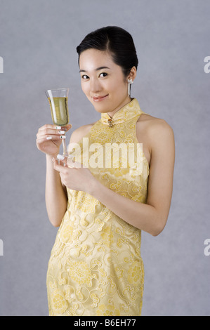 Jeune femme dans un cheongsam brodé jaune tenant une coupe de champagne Banque D'Images