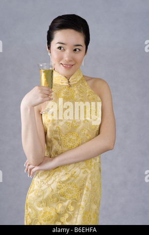 Jeune femme portant un cheongsam brodé jaune tenant une coupe de champagne Banque D'Images