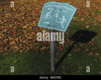 Signer avec lettrage 'Schont unsere Anlagen - Pièces nos locaux' debout sur une prairie avec beaucoup de feuilles d'automne liste forbidd Banque D'Images