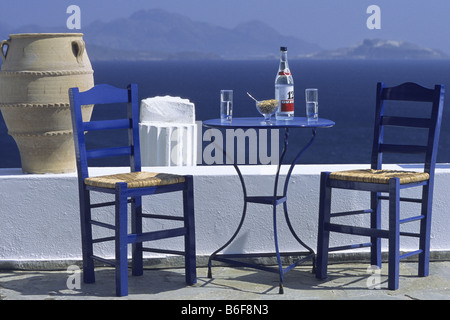 Chaises bleues et table avec bouteille d'Ouzo en face de mur blanc, de la Méditerranée en arrière-plan, la Grèce, le KOS Banque D'Images