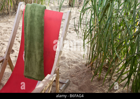 Chaise longue rouge avec une serviette verte sur une plage Banque D'Images