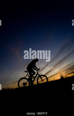 Young woman riding a bike, vtt, silhouette en face de ciel du soir Banque D'Images