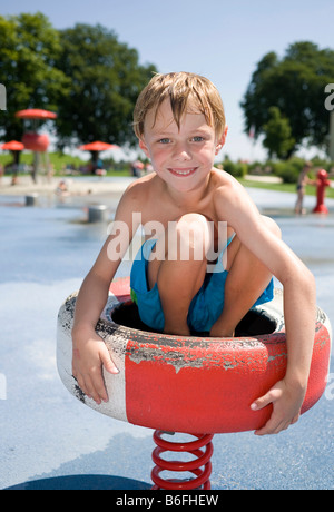 Garçon, 6 ans, assis sur un morceau de l'équipement de terrain dans un parc de l'eau Banque D'Images