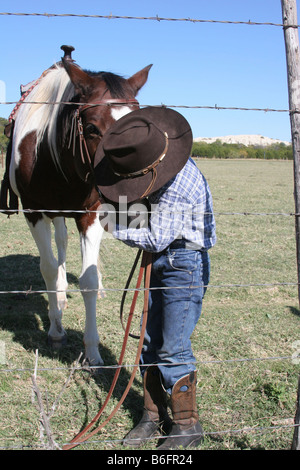 Un jeune cow-boy kissing son cheval sur le ranch à l'intérieur de l'Alpage Banque D'Images