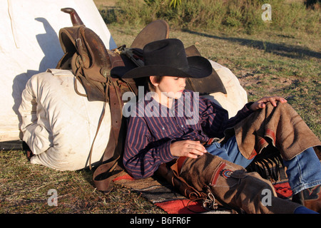 Un jeune cowboy en appui sur son lit de camp sur la plage Banque D'Images