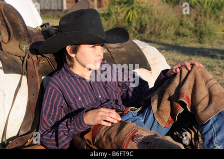 Un jeune cowboy en appui sur son lit de camp Banque D'Images