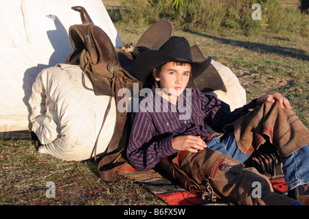 Un jeune cowboy en appui sur son lit de camp sur la plage Banque D'Images