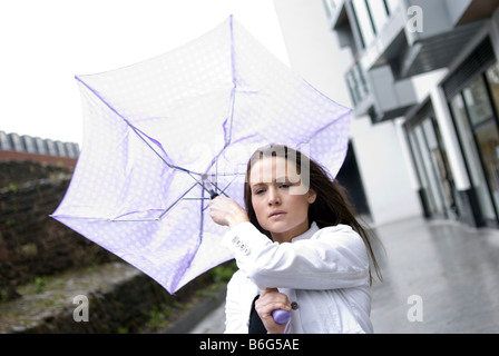 Jeune femme séduisante du mal comme son parapluie est soufflée autour dans le vent un jour de pluie Banque D'Images