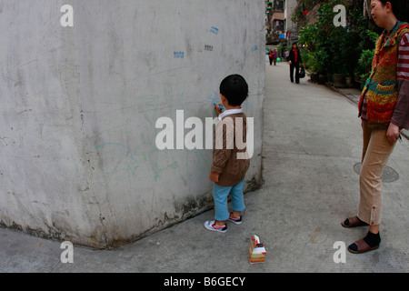 Jeune enfant chinois payer à l'extérieur faisant des dessins sur le mur Banque D'Images