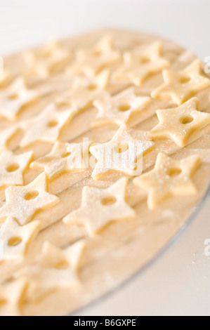 Biscuits au gingembre en forme d'étoiles portées sur le papier avant la cuisson. Découpe de petits trous pour insérer le ruban cependant. Banque D'Images