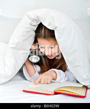 Girl reading sous couverture avec lampe Banque D'Images